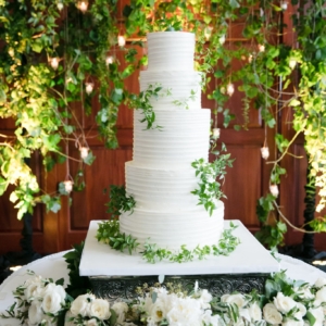 Kim starr wise floral event designer decorates wedding cake table and backdrop with vines and lush greenery