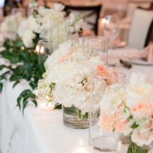 Various table centerpieces at the upscale new orleans wedding reception had lush arrangement of pave of all white, ivory and champagne and blush florals displayed in a clear vase lots of spring flowers in shades of white and ivory like tulips, hyacinths, ranunculus, iris, orlaya by kim starr wise event florist