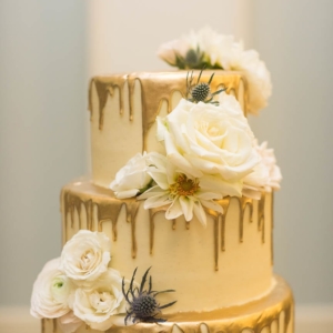 5 tier wedding cake with gold dripping down each tier accented with clusters of coordinating flowers and foliage by the kim starr wise floral design team in new orleans louisiana