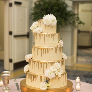 5 tier wedding cake with gold dripping down each tier accented with clusters of coordinating flowers and foliage by the kim starr wise floral design team in new orleans louisiana