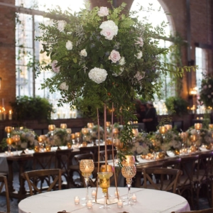 A tall wild heavy foliage arrangement in a gold vase display at wedding reception floral design by kim starr wise event florist in new orleans louisiana