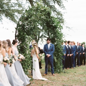 the bride and groom got married underneath a large arch covered with greenery and vines overlooking the gulf coast in mississippi