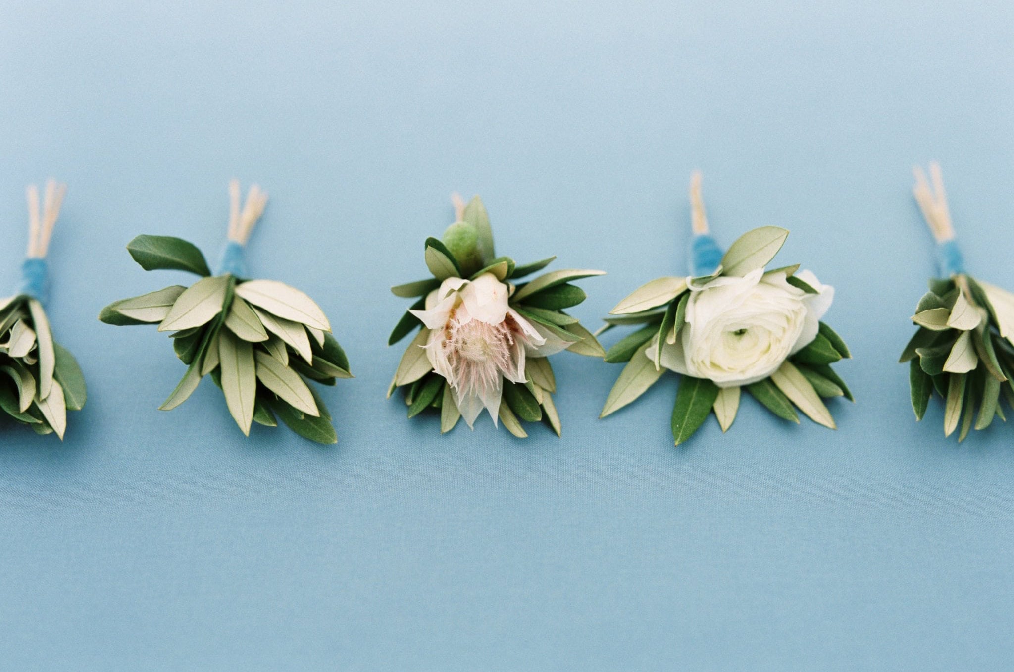 simple variety of tasteful green and white boutonnieres for the groomsmen and ushers at mississippi gulf coast wedding by kim starr wise white ranunculus boutonniere
